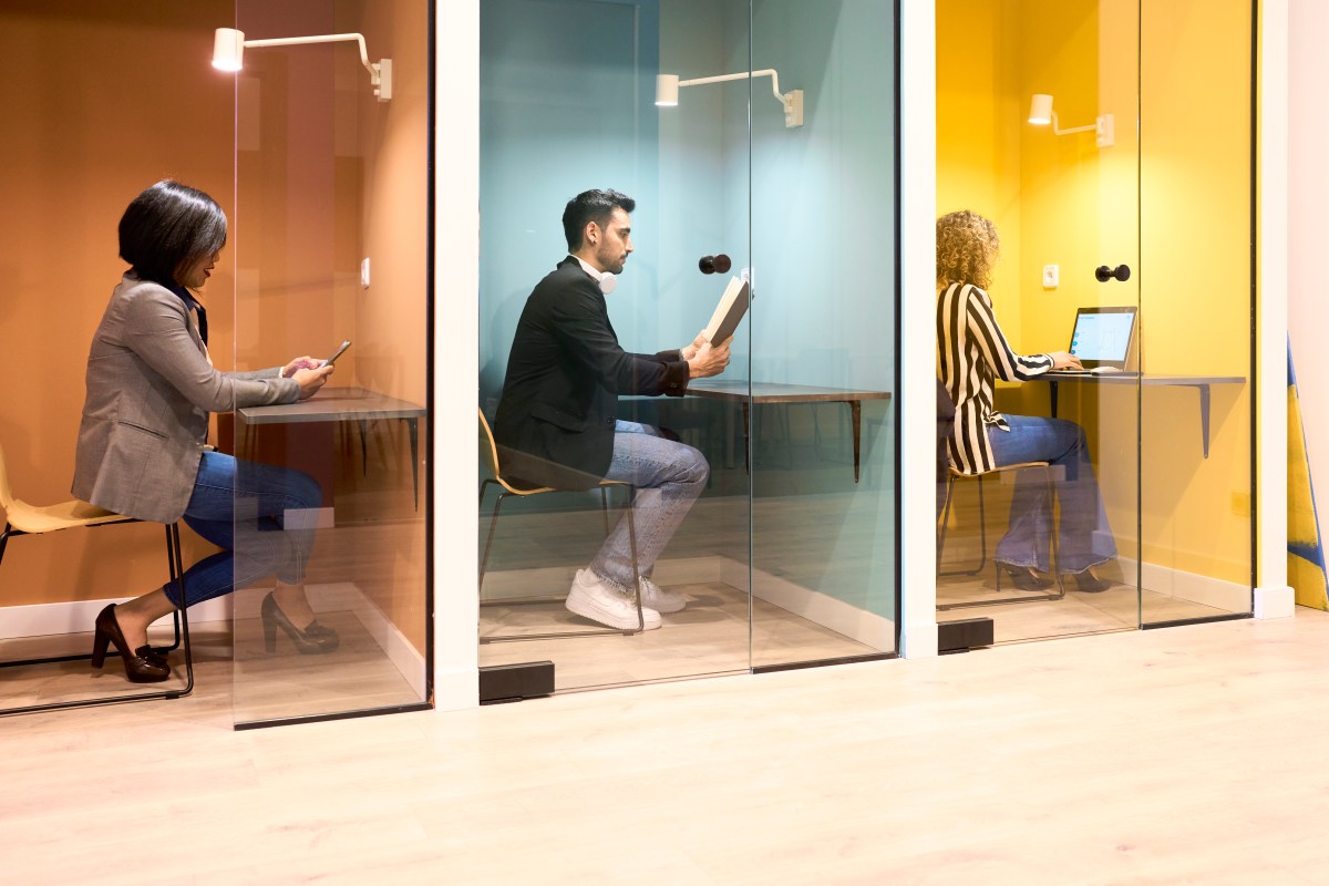 Train coworkers each sitting at the desk in their office cabin with a glass door, working