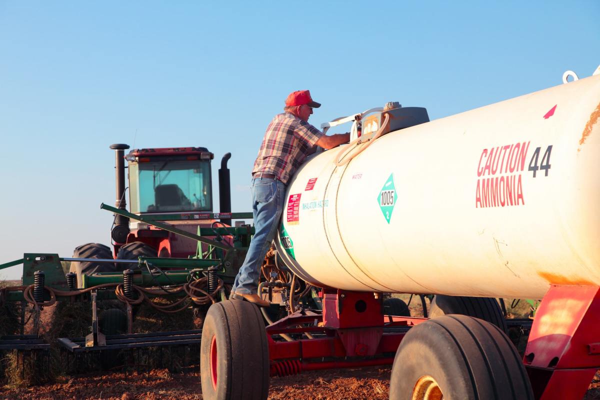 A farmer checks an ammonia tank hooked up to a tractor.