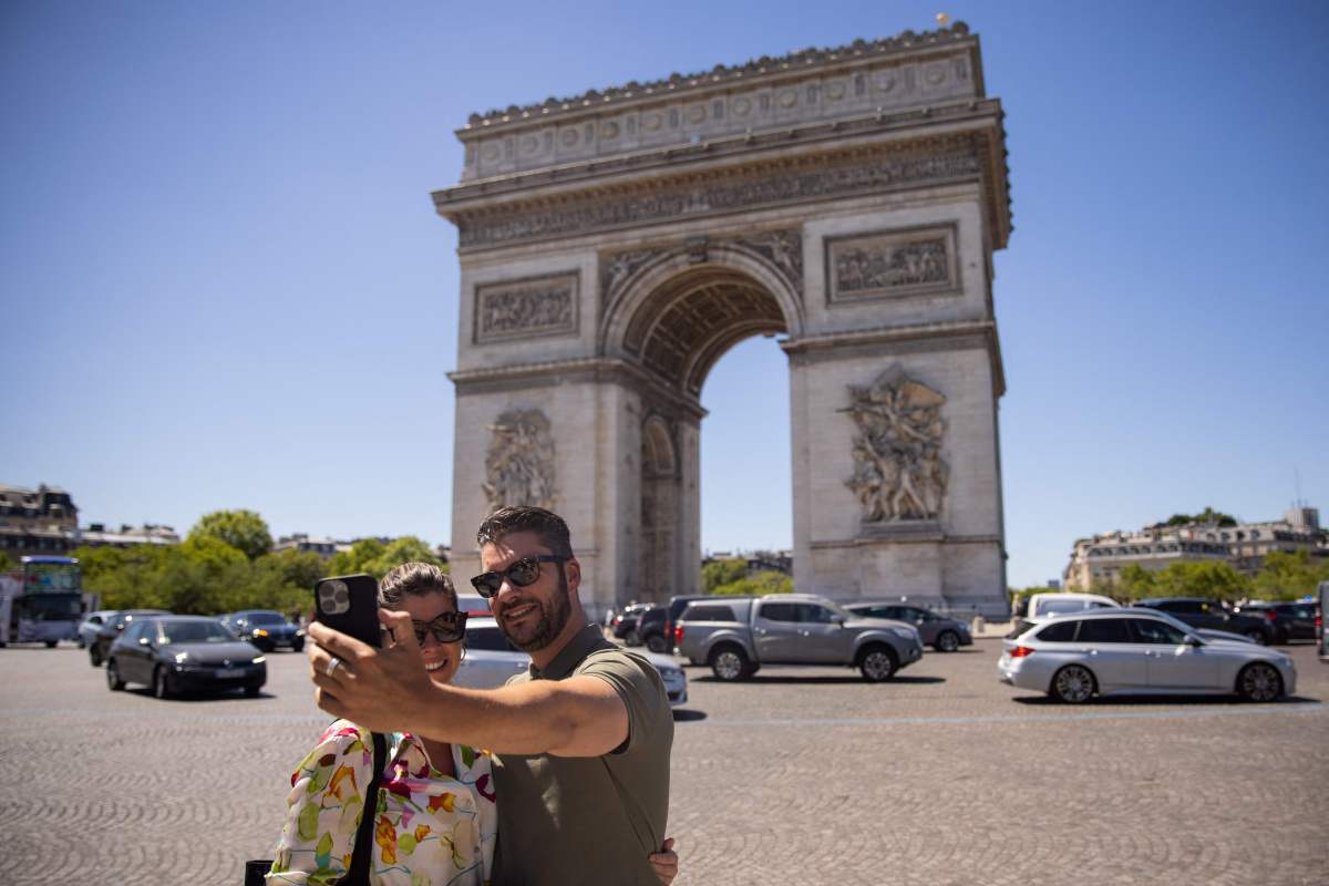 Tourists take selfie pictures in front of the Arc de Triomphe in Paris.